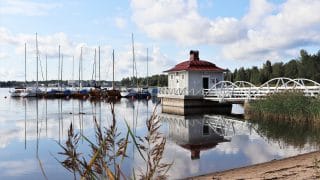Rannalta päin otettu kuva nuorisokeskus Villa Elban laiturisaunasta. Saunan takana venelaiturissa on lukuisia purjeveneitä. Taustalla olevalla vastarannalla näkyy metsää.