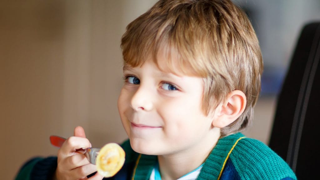 A little boy looks straight at the camera and has a fork in hand.