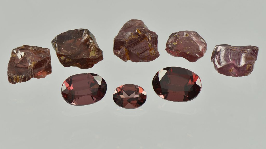 Garnets from Lemmenjoki as raw stones and faceted gemstones.
