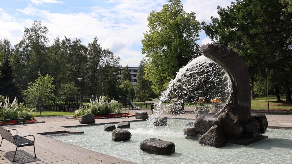 Länsipuistossa oleva Tyrsky -suihkukaivo, joka suihkuttaa vettä ympärillään olevaan altaaseen. Suihkukaivon takana avautuu Länsipuisto puineen.