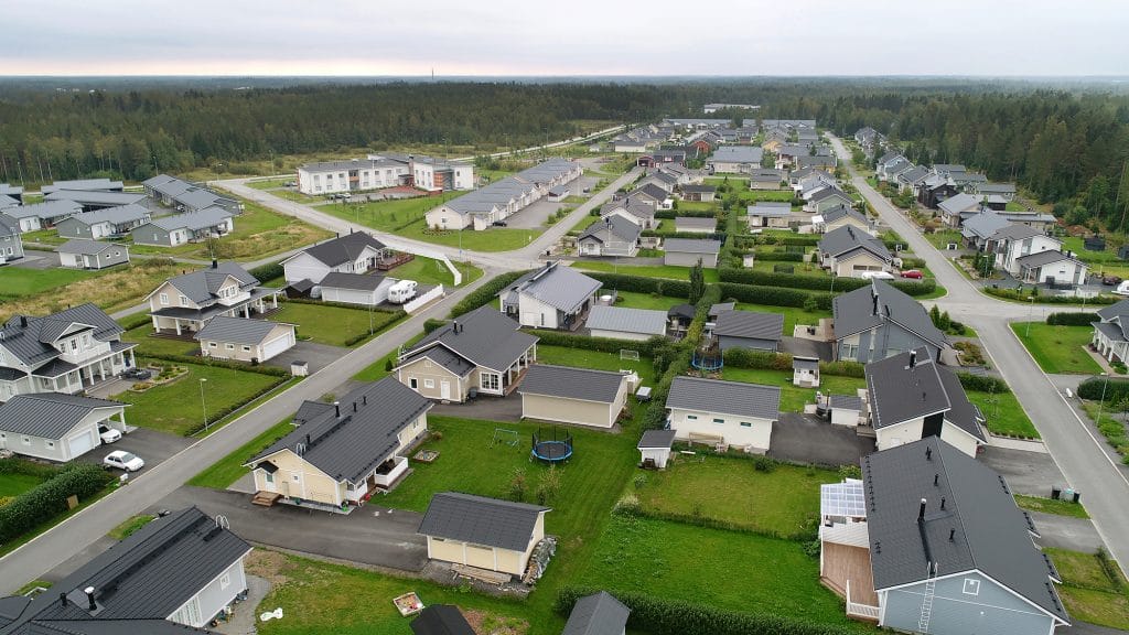 Ylhäältä kuvattu näkymä Puntusharjun asuinalueesta, joka koostuu enimmäkseen omakotitaloista vihreine pihoineen. Alueen takana levittäytyy metsä ja sen takana siintää etäisenä meri.