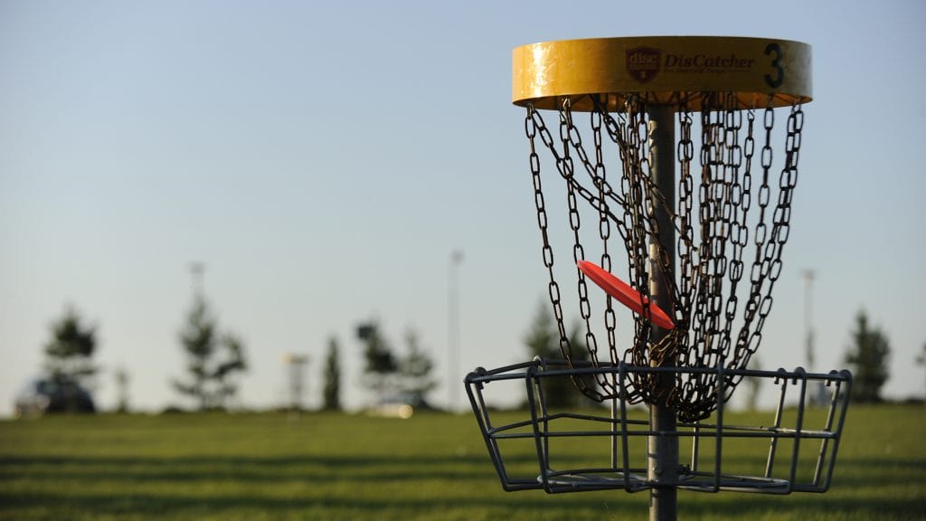 Frisbeegolfkorg på nära håll. En röd frisbee har precis landat i kedjorna i korgen med gul kant.