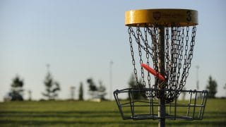 Frisbeegolfkori lähietäisyydeltä kuvattuna. Keltaisella reunalla varustetun korin ketjuihin on juuri lentänyt punainen frisbee.