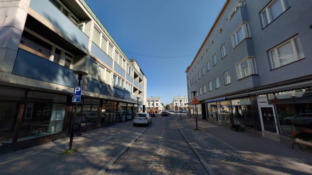 Näkymä Isokadulta, jossa molemmilla puolin katua matalia kerrostaloja. Kerrostalojen katutasossa on liiketiloja ja ylemmissä kerroksissa asuntoja. Kadun keskiosa on tehty mukulakivistä ja sen reunamilla on pysäköintipaikkoja kadun molemmin puolin. Taustalla etäisenä näkyy Mannerheiminaukio.
