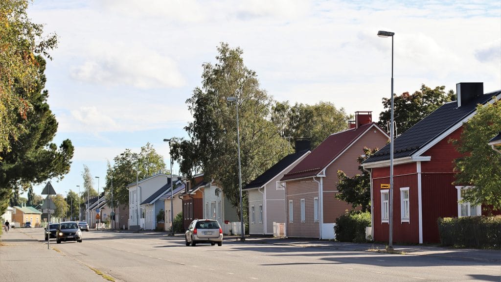 Katunäkymä Kustaa Aadolfinkadulta. Kuvan etualalla kulkee kaksisuuntainen tie, jossa kulkee useita autoja. Kuvan oikeassa reunassa, tien takana näkyy monenvärisiä rintamamiestaloja ja niiden pihoissa kasvavia lehtipuita.