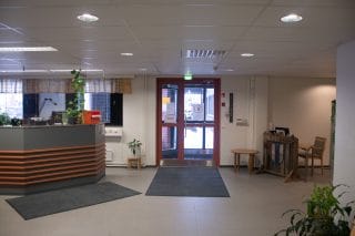 Aulatila sisältä kuvattuna. Vasemmalla asiakaspalvelutiski ja sen oikealla puolella ulko-ovi.