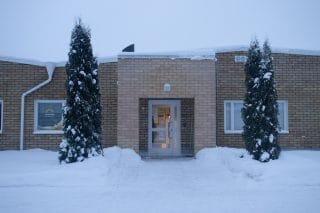 Keltaisen tiilirakennuksen sisäänkäynti, jonka molemmin puolin kaksi pylvästuijaa.